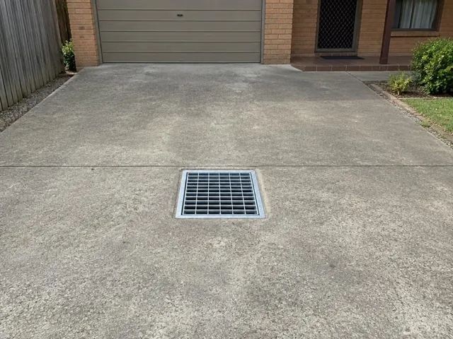 Concrete driveway with a clean square drain grate and garage entrance in Woodcroft